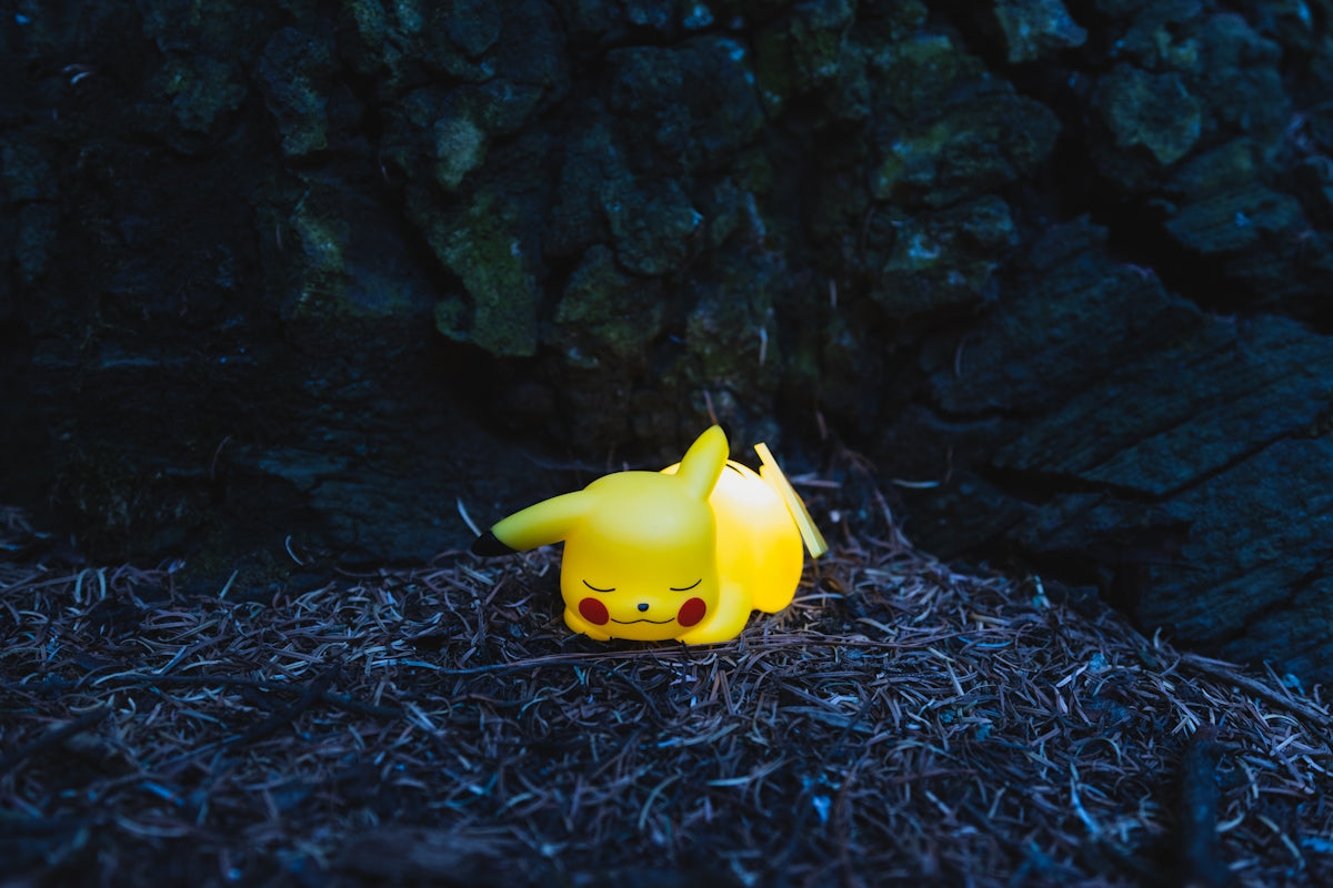 a pikachu figurine sitting on the ground next to a tree