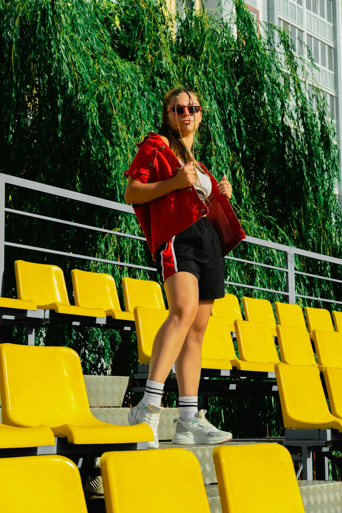 A woman in a red shirt and black shorts standing in front of a yellow stadium