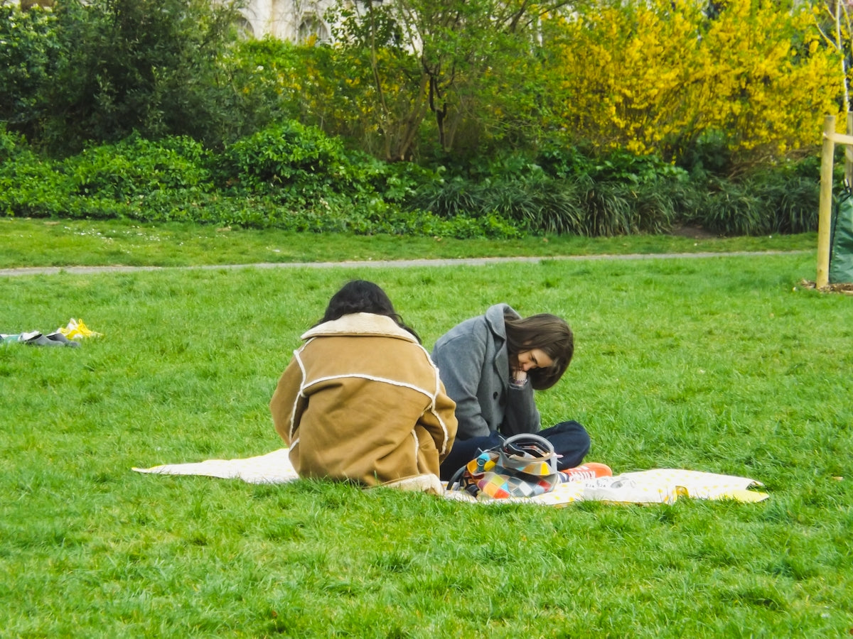 Two people are sitting on a blanket in the grass.