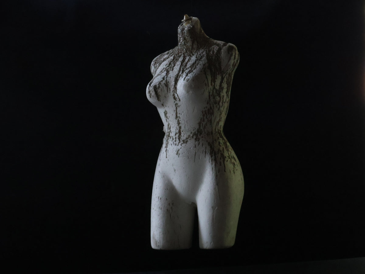A decayed statue stands against a dark background.