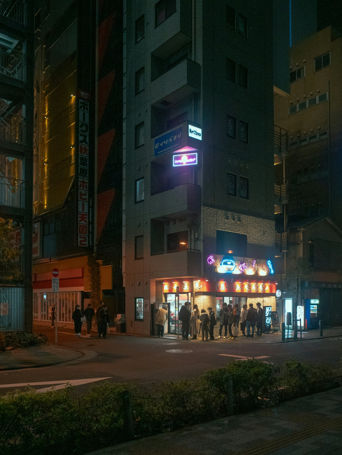 People queue outside a brightly lit building at night.